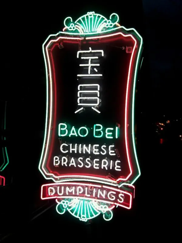 Red and green neon sign for Bao Bei Chinese Brasserie, with Chinese characters and a Dumplings banner, glowing at night